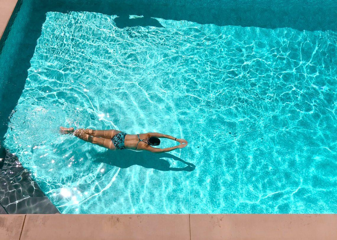 A woman in a swimming costume floating face down in a sunlit pool
