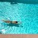 A woman in a swimming costume floating face down in a sunlit pool