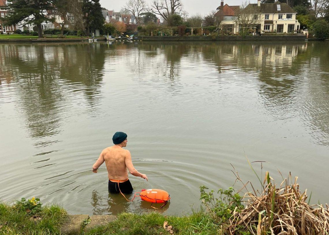 A man in jammers getting into a river, back to the camera