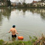 A man in jammers getting into a river, back to the camera