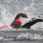 Close up of two swimmers in open water. The one nearest the camera has their head up looking forward.