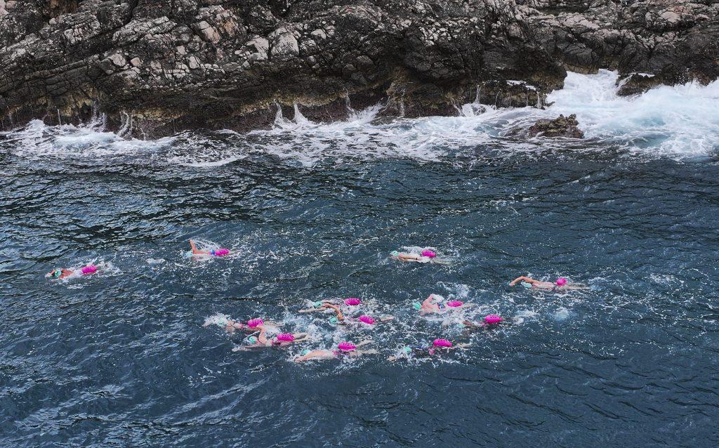 Swimmers swimming alongside a cliff in rough water