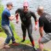 A person in a wetsuit getting out of the Jubilee River supported by two helpers
