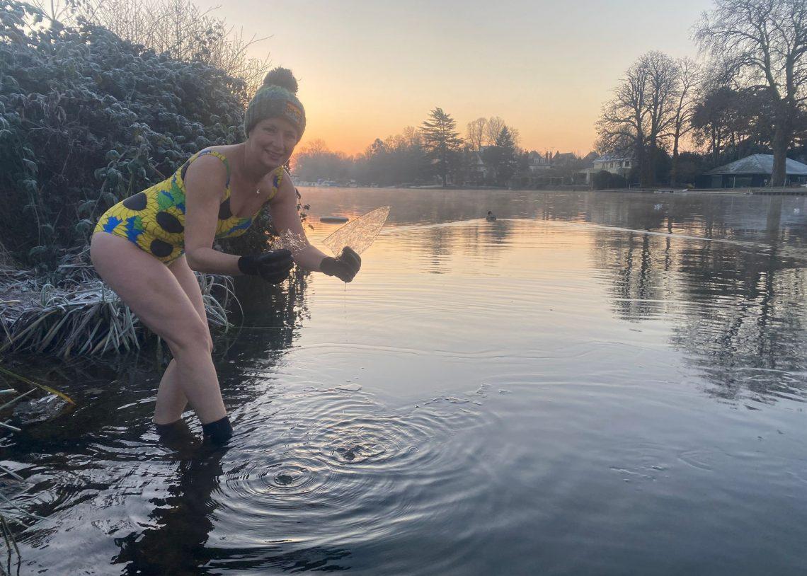 A woman in a swimming costume picks up a piece of ice from the Thames at sunrise
