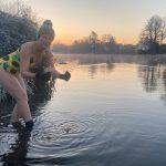 A woman in a swimming costume picks up a piece of ice from the Thames at sunrise