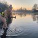 A woman in a swimming costume picks up a piece of ice from the Thames at sunrise