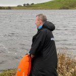 A man in a Dryrobe standing next to a lake