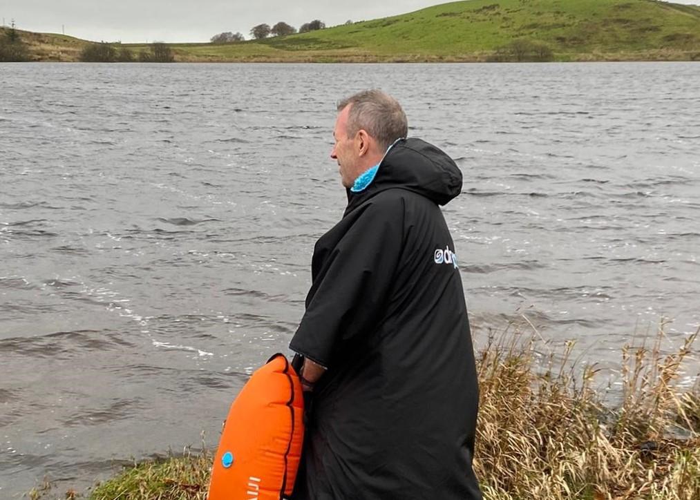 A man in a Dryrobe standing next to a lake