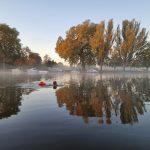 A swimmer in a river in autumn. The trees on the opposite bank in full autumn colours are reflected in the water.
