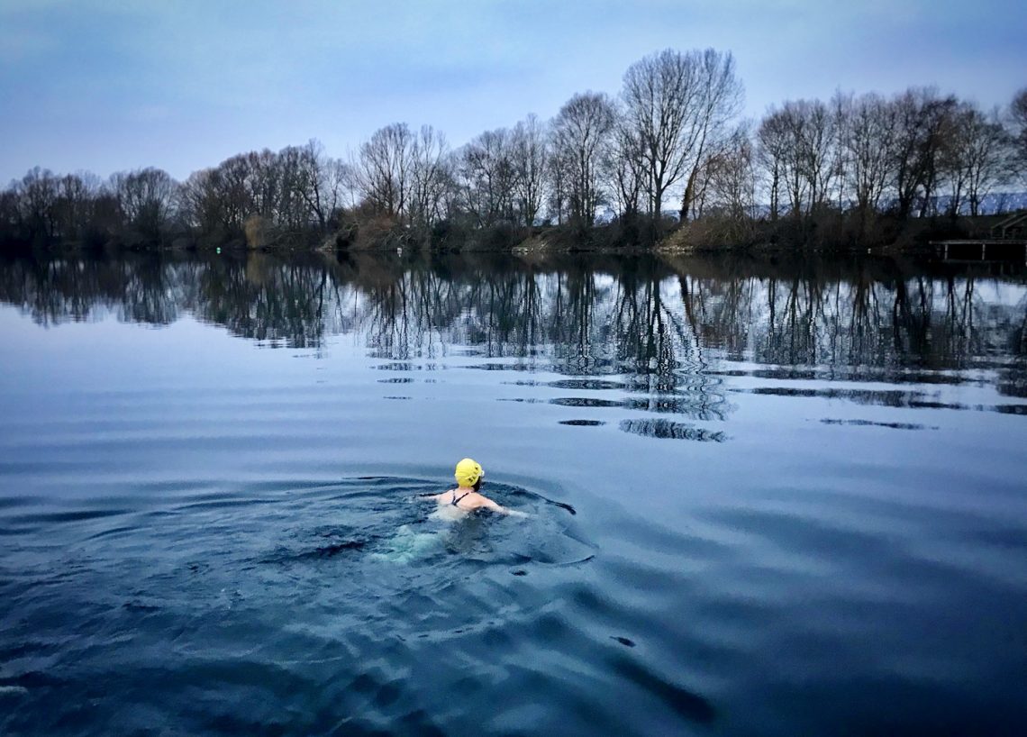 A swimming in a lake in winter doing breaststroke away from the camera