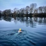 A swimming in a lake in winter doing breaststroke away from the camera
