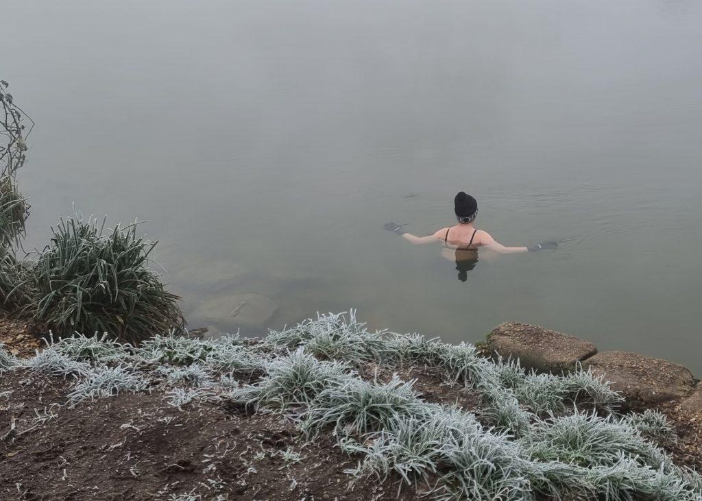 A woman standing neck deep in a river, facing away from the camera.